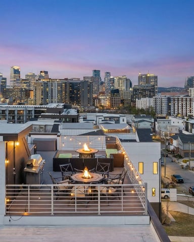 Modern rooftop deck with fire pit and city skyline at dusk, illuminated windows and downtown buildings in background