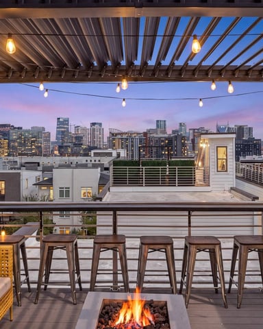 Modern rooftop deck with fire pit and city skyline at dusk, illuminated windows and downtown buildings in background